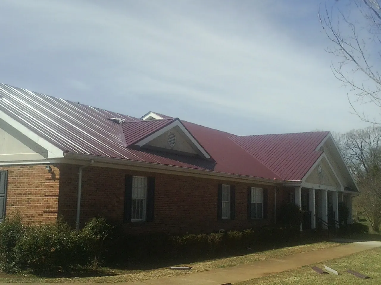 Red metal roof with gabled entries on a long brick building, from a Hail Damage Roof Repair job in Lempster
