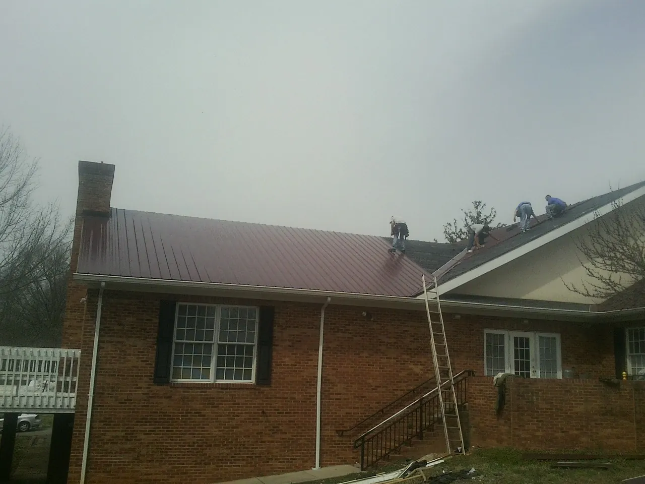 Crew setting red metal roofing panels on a brick home in Lempster