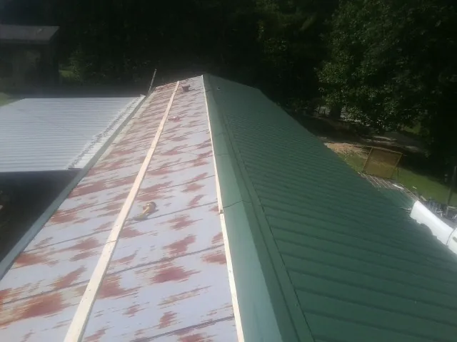 Old rusted panels beside newly installed green metal roofing — Wind Damage Roof Repair by Roofing Brothers in Lempster
