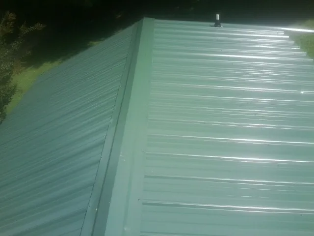 New green metal panels meeting at the ridge of a roof — Flat Roof Repair work by our crew in Lempster