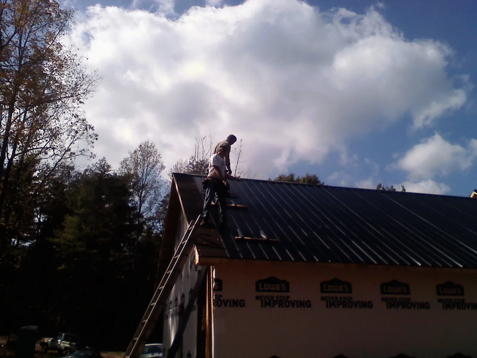 Roofer fastening dark metal panels high against a cloudy sky, from a Roof Inspection job in Lempster