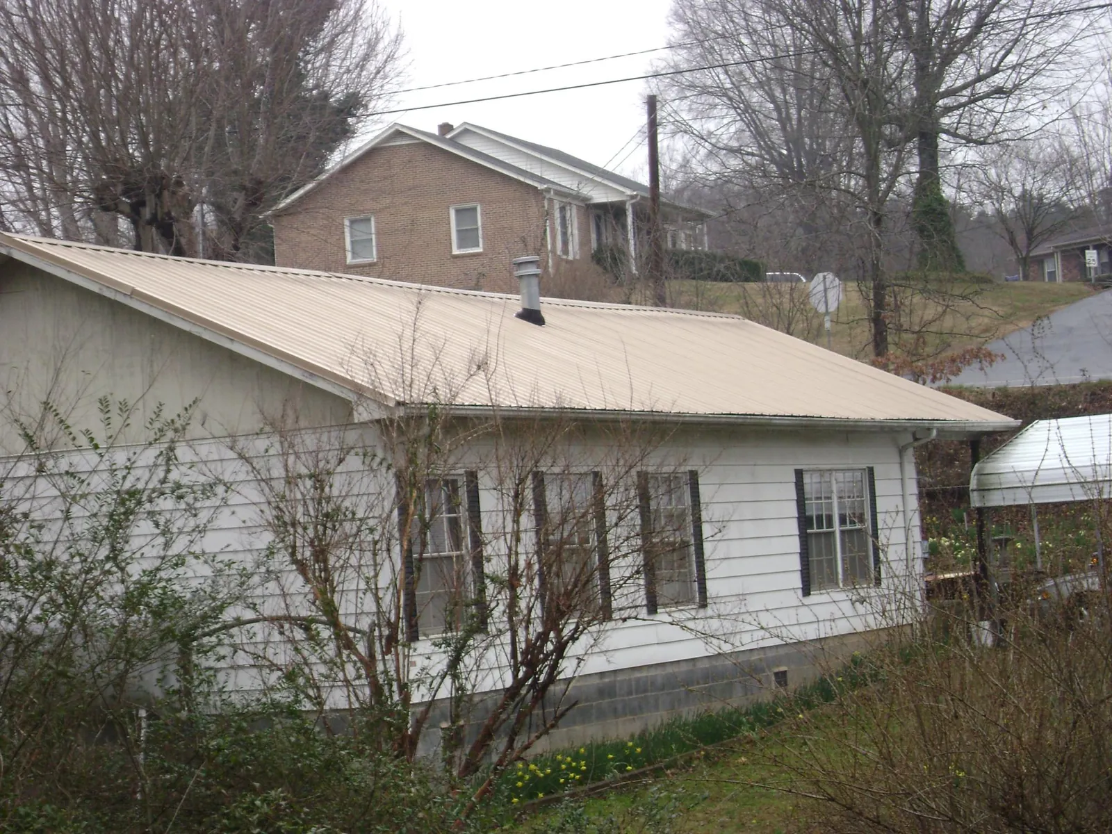 Tan metal roof on a white sided house set into a hillside — Commercial Roofing by Roofing Brothers in Lempster