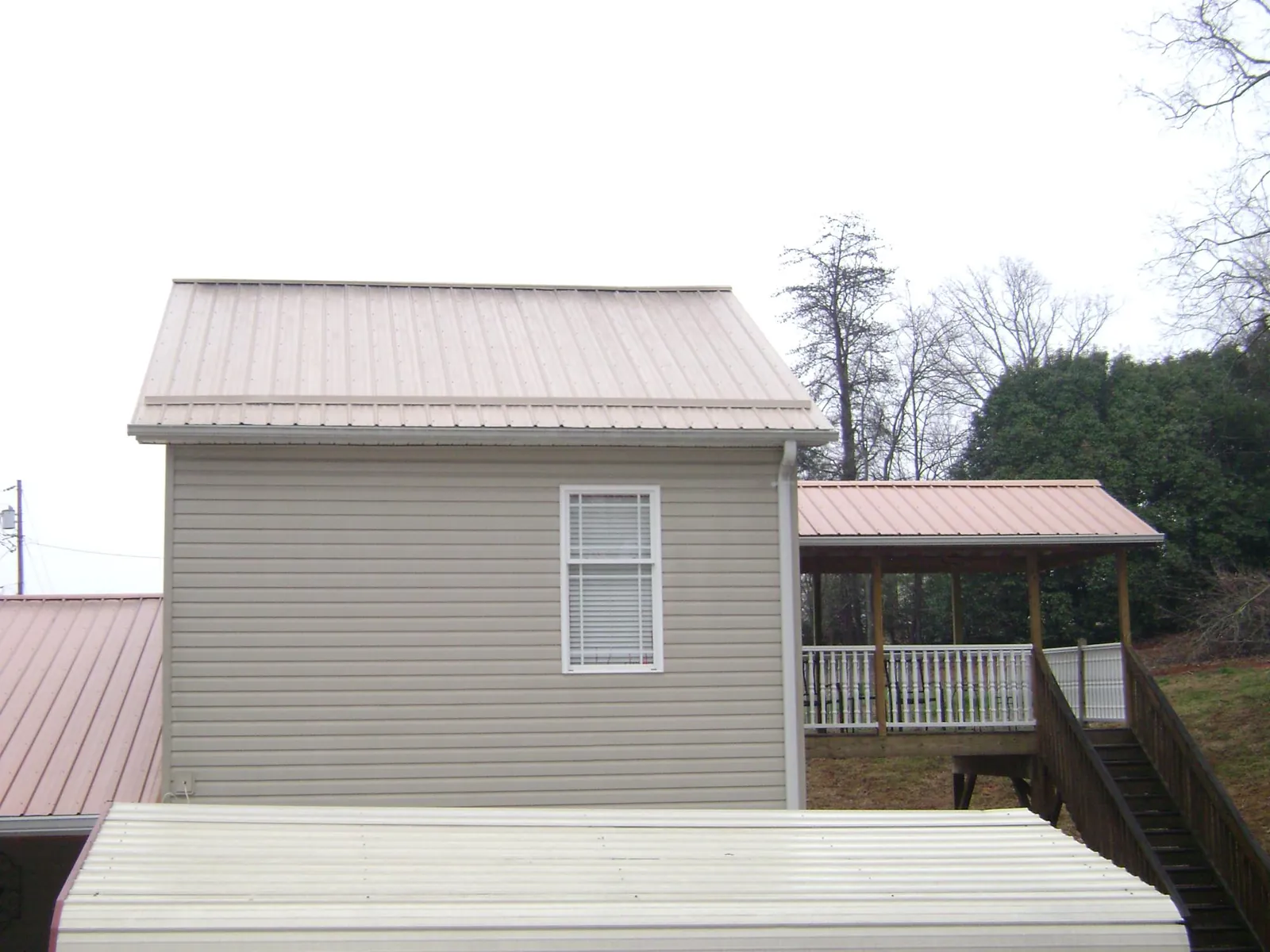 Tan metal roofs on a two story addition and attached porch, from a Roof Replacement job in Lempster